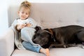 a little blonde girl at home on the sofa with a mobile phone and a big dog, children and gadgets