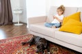 a little blonde girl at home on the sofa with a mobile phone and a big dog, children and gadgets