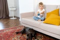 a little blonde girl at home on the sofa with a mobile phone and a big dog, children and gadgets