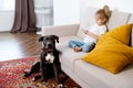 a little blonde girl at home on the sofa with a mobile phone and a big dog, children and gadgets