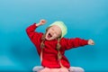 Little blonde girl, she laughing, sitting on floor, posing isolated on blue. Childhood, fashion Royalty Free Stock Photo