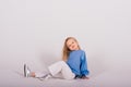 Little blonde girl, she laughing, sitting on floor, posing isolated on blue. Childhood, fashion Royalty Free Stock Photo