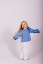 Little blonde girl, she laughing, sitting on floor, posing isolated on blue. Childhood, fashion Royalty Free Stock Photo