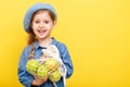 A little blonde girl with long hair in a blue dress and beret on a yellow isolated background. Child with apples.