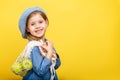 A little blonde girl with long hair in a blue dress and beret on a yellow isolated background. Child with apples.