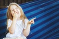 little blonde girl with long hair eats a strawberry in the garden sitting in a blue hammock Royalty Free Stock Photo