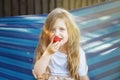 Little blonde girl with long hair eats a strawberry in the garden sitting in a blue hammock Royalty Free Stock Photo