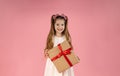 a little blonde girl with long hair holds a gift in her hands and smiles on a pink background. The girl looks out from Royalty Free Stock Photo