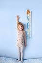 Little blonde girl measuring height against wall in room