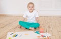 Little blonde girl paints on big white paper sitting on the floor indoors