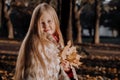 Little blonde girl in a plaid whip in the park in autumn Royalty Free Stock Photo