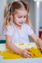 Little blonde girl play with yellow magic sand on white glowing table. Sensory development. Lessons in kindergarten