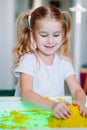 Little blonde girl play with yellow magic sand on white glowing table. Sensory development. Lessons in kindergarten