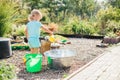 Little blonde girl playing at garden with water in a tin basin. Kids gardening. Summer outdoor water fun. Childhood in the country Royalty Free Stock Photo