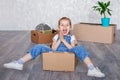 A little blonde girl plays at home in quarantine with cardboard boxes. The child moves to a new apartment, is happy and