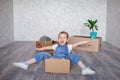 A little blonde girl plays at home in quarantine with cardboard boxes. The child moves to a new apartment, is happy and