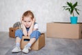 A little blonde girl plays at home in quarantine with cardboard boxes. The child moves to a new apartment, is happy and