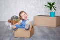 A little blonde girl plays at home in quarantine with cardboard boxes. The child moves to a new apartment, is happy and