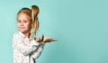 Little blonde girl with ponytail, in shirt with hearts print. She smiling, holding something posing on blue background. Close up Royalty Free Stock Photo