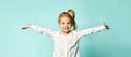 Little blonde girl with ponytail, in shirt with hearts print. She smiling, spread her hands, posing on blue background. Close up Royalty Free Stock Photo