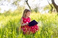 Little blonde girl in a red dress reads a book with fairy tales in nature Royalty Free Stock Photo