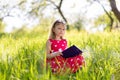 Little blonde girl in a red dress reads a book with fairy tales in nature Royalty Free Stock Photo