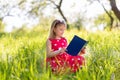 Little blonde girl in a red dress reads a book with fairy tales in nature Royalty Free Stock Photo