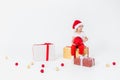 Little blonde girl in red santa hat sitting on a gift box with big red ball in her hands on a white background