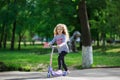 Little blonde girl ride the scooter in the park. Royalty Free Stock Photo