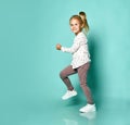 Little blonde girl in shirt with hearts print, checkered pants, white sneakers. Smiling, dancing on blue background. Full length Royalty Free Stock Photo