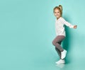 Little blonde girl in shirt with hearts print, checkered pants, white sneakers. Smiling, dancing on blue background. Full length Royalty Free Stock Photo