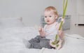 Little blonde girl sitting on the bed in a light top and gray pants with pink flowers Royalty Free Stock Photo