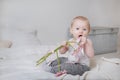 Blonde girl sitting on a bed with pink flowers and ribbon, portrait of a cute baby on a light background Royalty Free Stock Photo