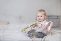 1 little blonde girl sitting on a bed with pink flowers and ribbon and smiling, portrait of a cute baby on a light