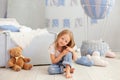 Little blonde girl is sitting on floor against background of decorative balloon. Smiling child plays in a children`s room with a t Royalty Free Stock Photo