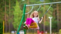 Little blonde girl smiling swinging outdoors on a playgroung