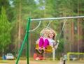 Little blonde girl smiling swinging outdoors on a playgroung