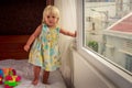 little blonde girl stands by window side-view Royalty Free Stock Photo