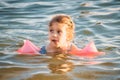 A little blonde girl swimming in the sea in summer wearing pink inflatable armbands Royalty Free Stock Photo