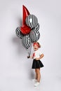 Little blonde girl in t-shirt, red headband, black skirt and sneakers. She holding balloons, posing isolated on white. Full length Royalty Free Stock Photo