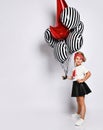 Little blonde girl in t-shirt, red headband, black skirt and sneakers. She holding balloons, posing isolated on white. Full length Royalty Free Stock Photo