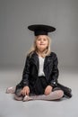 Little blonde girl in a white dress and black leather jacket is posing standing over a gray background. Royalty Free Stock Photo
