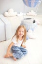 Little blonde girl in a white T-shirt and jeans sits near a decorative balloon. Funny kid plays near the balloon in the children`s Royalty Free Stock Photo
