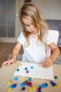 Little blonde girl in a white tshirt playing with plastic multicolor mosaic at home or preschool. Early education concept