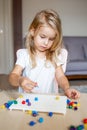 Little blonde girl in a white tshirt playing with plastic multicolor mosaic at home or preschool. Early education concept