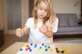 Little blonde girl in a white tshirt playing with plastic multicolor mosaic at home or preschool. Early education concept.