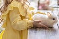 A little blonde girl in a yellow dress is sitting at a festive Easter table with rabbits.A baby and a rabbit. The concept of