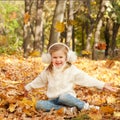 Little blonde happy girl sitting on autumn yellow maple leaves and smiling, play outdoor in autumn park Royalty Free Stock Photo