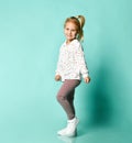 Little blonde kid in shirt with hearts print, checkered pants, white sneakers. Smiling, dancing on blue background. Full length Royalty Free Stock Photo