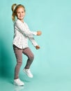 Little blonde kid in shirt with hearts print, checkered pants, white sneakers. Smiling, dancing on blue background. Full length Royalty Free Stock Photo